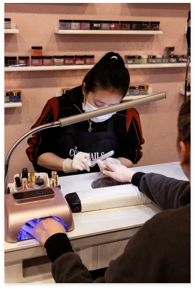 Nail technician working at her station with shelves of SNS powder jars behind