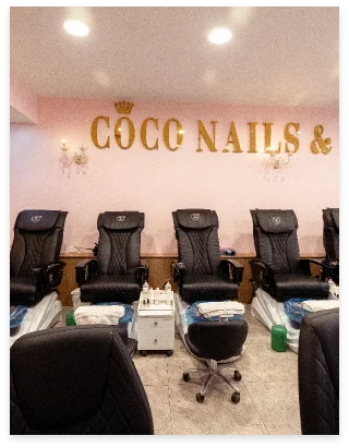 Pedicure lounge with black massage chairs beneath gold CoCo Nails crown lettering on a blush wall